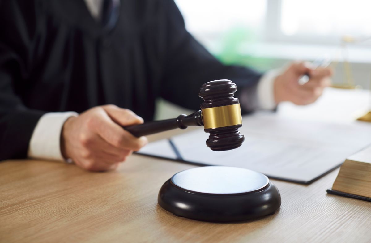 Man judge knocking gavel wearing robe having court verdict sitting at the desk on workplace in courtroom. Closeup of male justice worker working indoors. Legal law and justice concept.