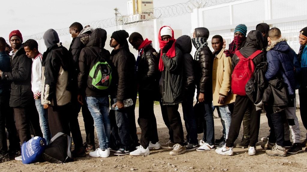 Hundreds of migrants wait for buses in the cold  in Calais, France, on October 28, 2016. There are still many men at the camp who are determined to get to the UK even as they leave the Jungle. The men claim they are being kept from their families who have lived in the UK for years and they want to be reunited with them. They also claim they are being refused entry to the UK because of a lot of prejudices and discrimination against them as migrants and refugees. (Photo by Gail Orenstein/NurPhoto) (Photo by Gail Orenstein / NurPhoto via AFP)