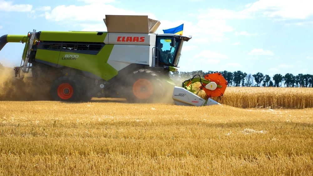 Kharkiv, Ukraine - Jule, 18, 2022: A harvester with the Ukrainian flag harvests wheat in the field. Collection of early grains in the conditions of the war between Ukraine and Russia