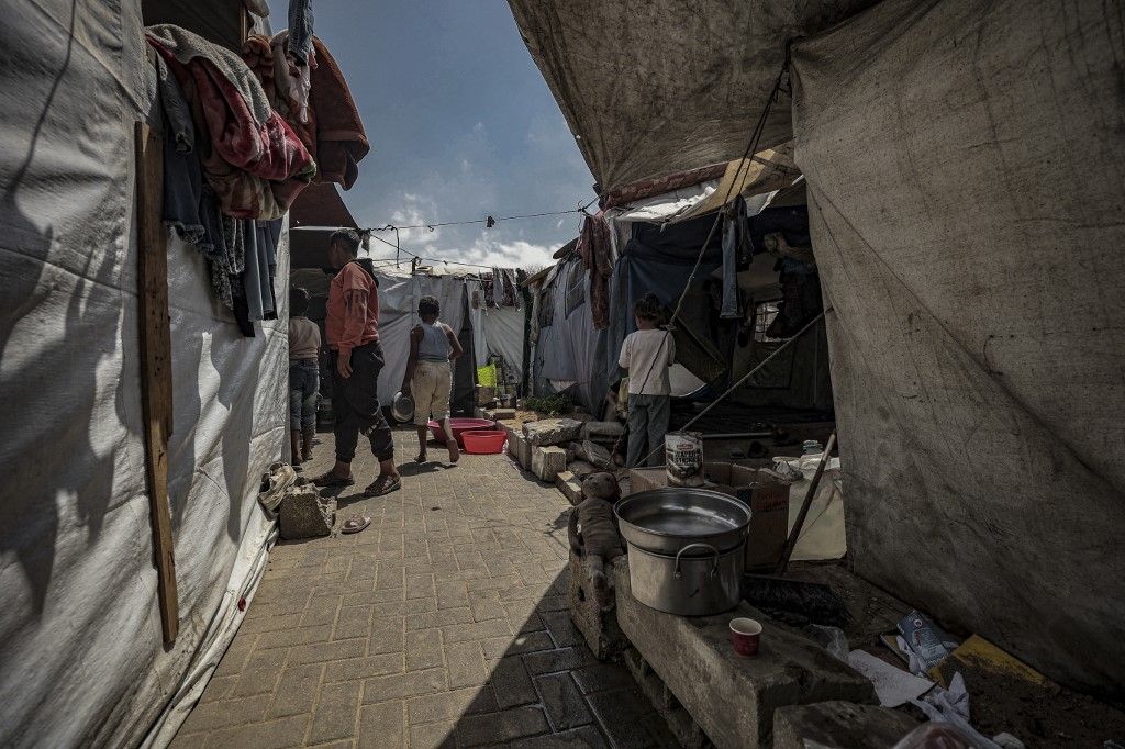 People walk among tents at a displacement camp in the Gaza Strip on May 20, 2026. Palestinians in Gaza are preparing for Eid al-Adha amid worsening humanitarian conditions and food shortages caused by the ongoing war, with many families unable to afford traditional holiday meals or sacrificial animals. (Photo by Abood Abusalama / Middle East Images via AFP)