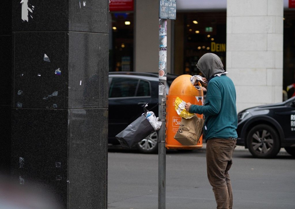 24 June 2025, Berlin: 24.06.2025, Berlin. A homeless woman wearing a hood searches a BSR waste basket for returnable bottles, cans and food in the city center. Photo: Wolfram Steinberg/dpa Photo: Wolfram Steinberg/dpa (Photo by Wolfram STEINBERG / dpa Picture-Alliance via AFP)