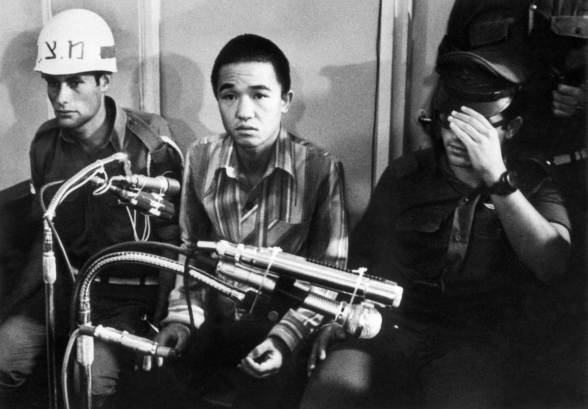 (FILES) This photo taken on July 10, 1972 shows Kozo Okamoto (C) -- the only surviving member of the three-man "Japanese Red Army" (JRA) commando unit that killed 26 people in an attack on Israel's Lod airport earlier on May 30 -- during the opening of his trial before a military tribunal at an undisclosed location in central Israel. Kozo Okamoto, who carried out a deadly attack on an Israeli airport on behalf of the Popular Front for the Liberation of Palestine, died on July 23, 2026 in Beirut aged 78, the group said. (Photo by AFP)