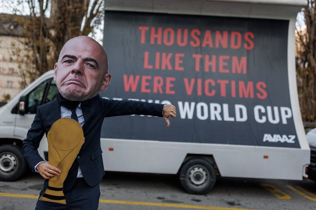 A man with a mask representing FIFA President Gianni Infantino and a football World Cup trophee gestures next to giant billboards in a street of Infantino's hometown of Brig, where his parents originally moved as migrants, during a protest by NGO Avaaz calling on Infantino to commit to a $440 million FIFA compensation fund for victims of this Qatar 2022 World Cup football tournament, on December 7, 2022. (Photo by VALENTIN FLAURAUD / AFP)