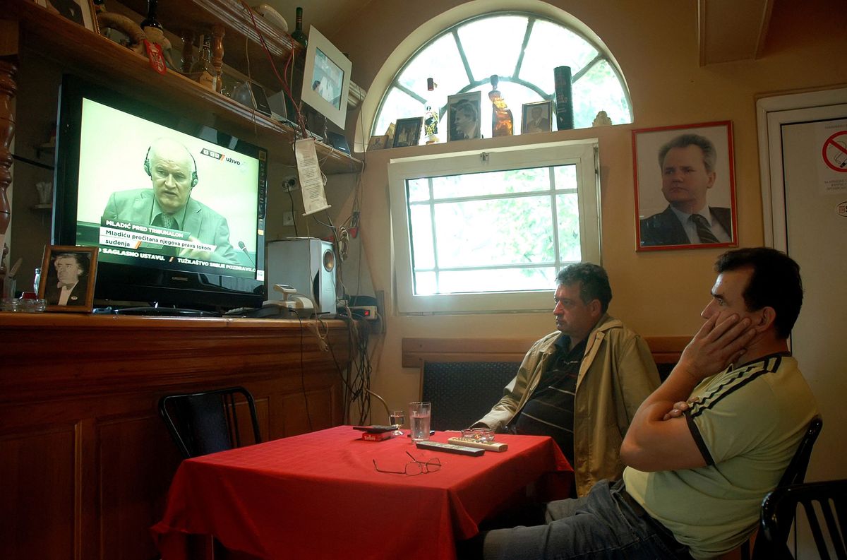 (FILES) Two men watch the live broadcast of wartime Bosnian Serb army chief Ratko Mladic's appearance before the International Criminal Tribunal for the former Yugoslavia in a coffee shop in Belgrade on June 3, 2011. Former Bosnian military Serb leader and war criminal Ratko Mladic has died in a prison hopsital in the Hague, according to Serbian state broadcaster RTS on August 27, 2026, after suffering several strokes. Mladic, 84, was dubbed the "Butcher of Bosnia" for his role in the 1995 Srebrenica massacre during the Bosnian war. (Photo by ALEKSANDAR JOVANOVIC / AFP)