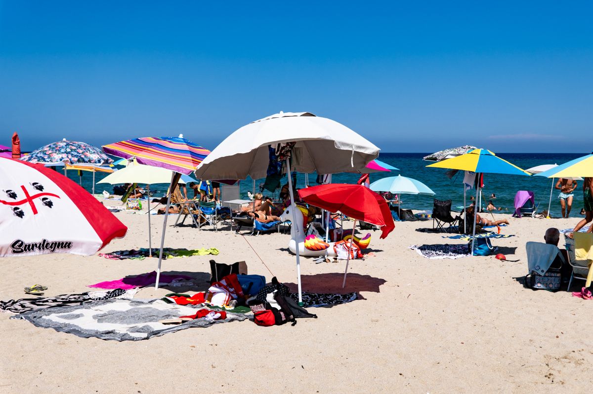 People are at the beach in Budoni, Sardinia, Italy, on August 7, 2026. In the distance, the profile of Tavolara island is visible. (Photo by Emmanuele Contini/NurPhoto) (Photo by Emmanuele Contini / NurPhoto via AFP)
