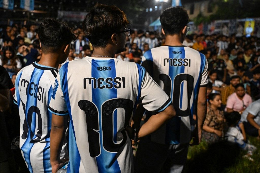 Football fans wearing the jersey of Argentina's Lionel Messi stand as they watch a live broadcast of the 2026 World Cup football tournament final match between Spain and Argentina on a screen at a public fan zone in Kolkata on July 20, 2026. (Photo by Dibyangshu SARKAR / AFP)