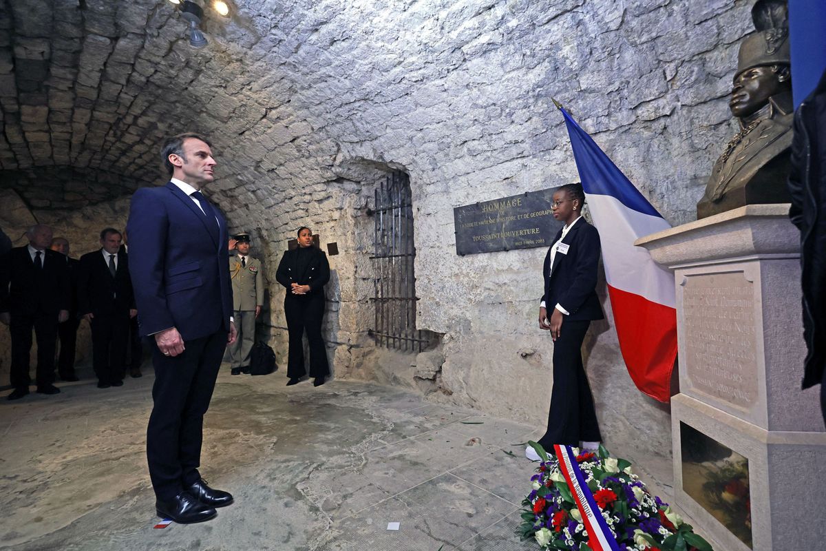 French President Emmanuel Macron (L) pays tribute in front of a statue of Toussaint Louverture, leader of the Haitian independence movement, before visiting the "Chateau de Joux" during a ceremony marking the 175th anniversary of the abolition of slavery in France, in La Cluze-et-Mijoux, near Besancon, eastern France, on April 27, 2023. Macron visited "Chateau de Joux" to pay tribute to mark the 220th anniversary of the death of Franco-Haitian general Toussaint Louverture at the site where he was imprisoned until his death. (Photo by Christophe PETIT TESSON / POOL / AFP)
