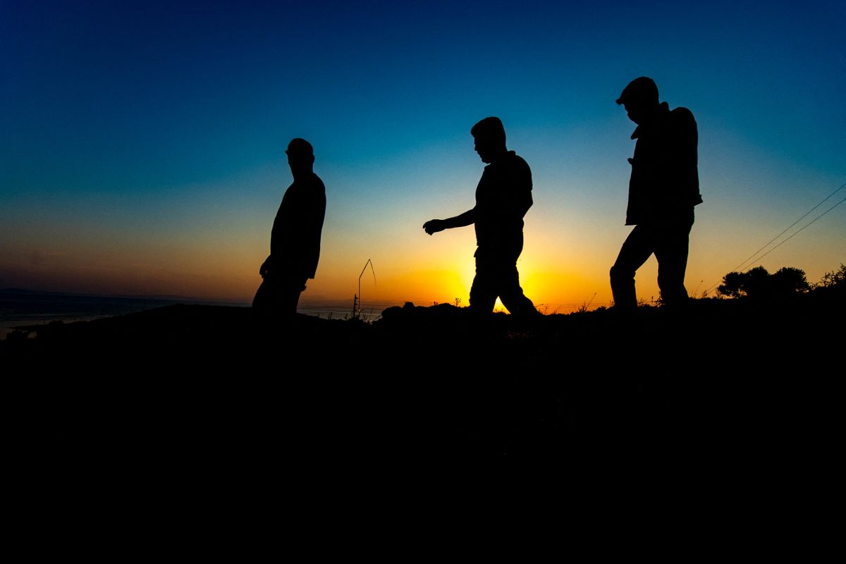 Group of male asylum seekers walk early in the morning towards Moria. Silhouettes of walking refugees and migrants on the hills early in the morning during the dawn and the sunrise over the Aegean sea and Turkey. Asylum seekers walk early in the morning before the daylight from the makeshift shelter with tents on the roadside near Kara Tepe and Mytilene city towards the burned Moria Refugee camp or hot spot to collect belongings and visit their makeshift shops that didn't burn, via the mountains on trails, as they don't want to be captured by the police and forced to enter and live in the new Temporary Refugee Camp of Kara Tepe that was built after the fire. Lesbos Island, Greece on September 21, 2020 (Photo by Nicolas Economou/NurPhoto) (Photo by Nicolas Economou / NurPhoto via AFP)