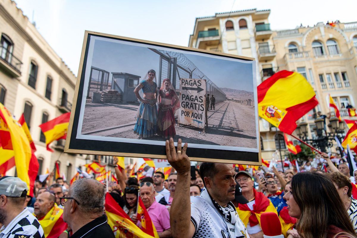 Protesters hold Spain's flags and a banner mocking Spain's Prime Minister Pedro Sanchez and Spain's Interior Minister Fernando Grande-Marlaska reading 'free entrance, this way' during a demonstration one month after a mass influx of migrants in Ceuta on September 2, 2026, the annual Ceuta Day. Local anger divide Ceuta one month after the mass influx of migrants into the North African Spanish territory. 5,000 migrants according to the government, or at least 10,000, according to Ceuta authorities, remain in the small territory of 18.5 square kilometers and 80,000 inhabitants, wandering the streets in search of food and sleeping in streets and on beaches. (Photo by Antonio Sempere / AFP)