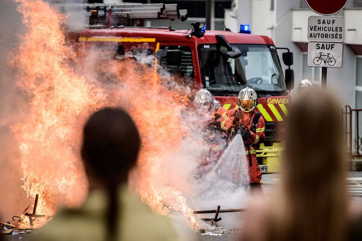 A firefighter sprays water onto a large street fire beside a fire engine during the high school protest in Pau, Pyrenees-Atlantiques, Nouvelle-Aquitaine, France, on 2 October 2026. The Pau action was part of a nationwide high school mobilization over school resources and study conditions, with disturbances around Lycee Saint-Cricq including burning bins, tear gas and arrests. (Photo by Quentin Top / Hans Lucas via AFP)