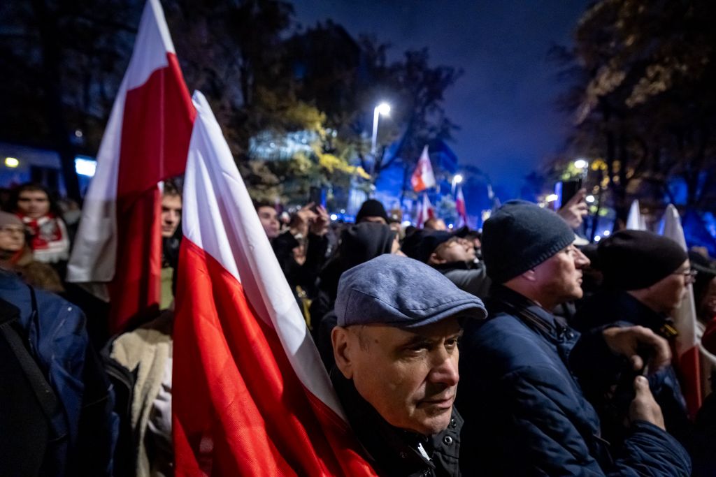 A man holding a Poland's national flag gathers with fellow protesters outside the headquarters of the Poland's Constitutional Court in Warsaw after police blocked access to the court building on October 30, 2026. Poland's President Karol Nawrocki called off a visit to Africa in mid-flight as riot police deployed around the country's constitutional court on October 30 following the suspension of its chief justice in a battle between the centrist government and the nationalist right. Dozens of police guarded the entrance to the court as followers of the opposition right-wing Law and Justice party (PiS) protested the ousting of constitutional court president Bogdan Swieczkowski. (Photo by Wojtek RADWANSKI / AFP)