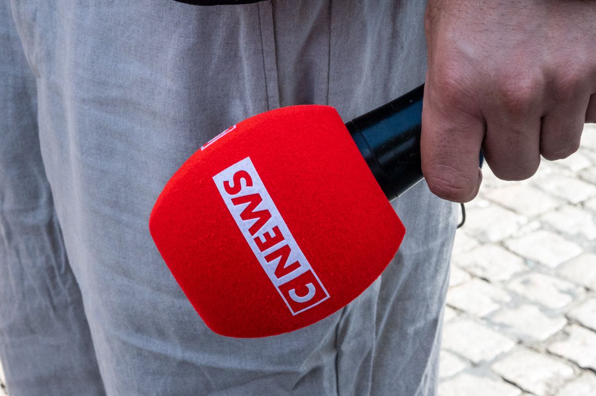 CNEWS handheld microphone in a street scene, with the red cover and white logo clearly visible against a background of cobblestones and light-colored clothing in Paris, France, on September 15, 2026. Journalist. (Photo by Riccardo Milani / Hans Lucas via AFP)
