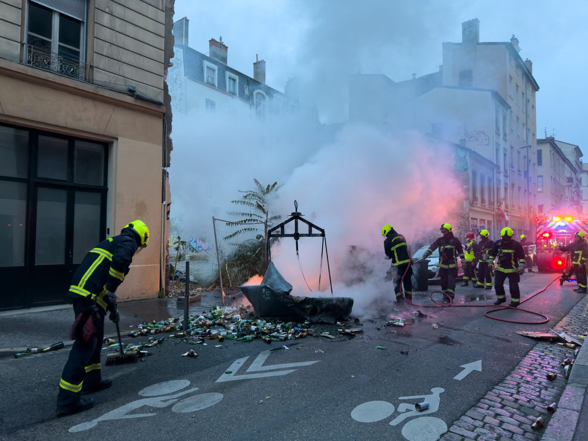 Firefighters extinguish a fire during a protest in Lyon, France on October 24, 2026. Authorities deployed around 70,000 security personnel across France for renewed protests over the cost of living, after unrest a week earlier saw public buildings damaged, hundreds of shops looted and about 2,700 people arrested. (Photo by Abolfazl Salmanzadeh / Middle East Images via AFP)