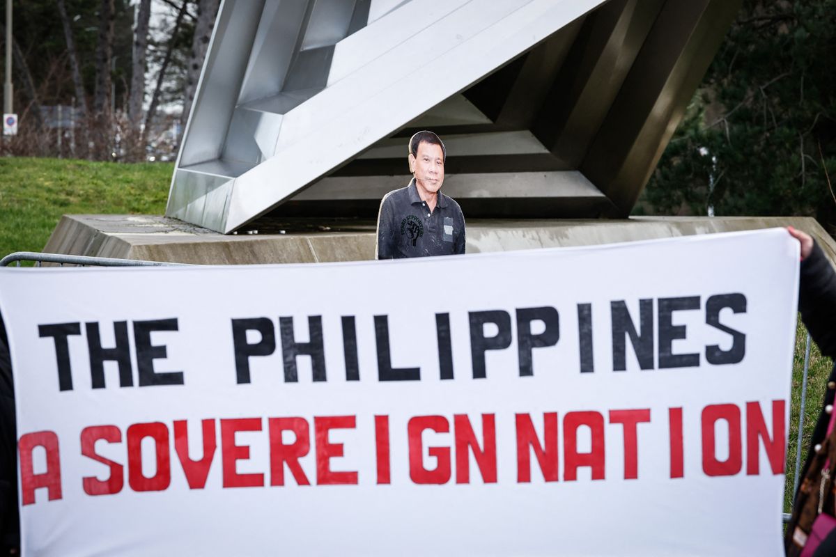 People hold a banner reading "The Philippines, A sovereign Nation" in front of a life-size cartboard cutout of former Philippines' president Rodrigo Duterte during a demonstration in his support outside the International Criminal Court (ICC) where he will be questioned on charges of crimes against humanity, in The Hague on February 23, 2026. As the 80-year-old will not be present at the hearing after the court granted a defence request to waive his right to appear, despite judges ruling that he was fit to take part, the "confirmation of charges" hearing, taking place over four days, will determine whether there is enough evidence against Duterte to proceed to a trial. (Photo by Simon Wohlfahrt / AFP)