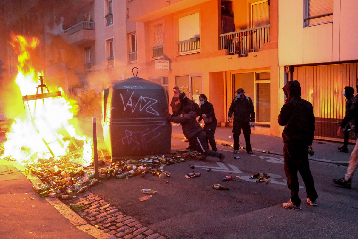 Masked protesters push a large rubbish container beside a burning barricade, with broken glass bottles scattered across the street, during clashes in Lyon, France, on October 24, 2026. Demonstrations continued despite restrictions imposed by authorities following unrest the previous weekend, with police using tear gas to disperse protesters and barricades set on fire in parts of the city. (Photo by Abolfazl Salmanzadeh / Middle East Images via AFP)